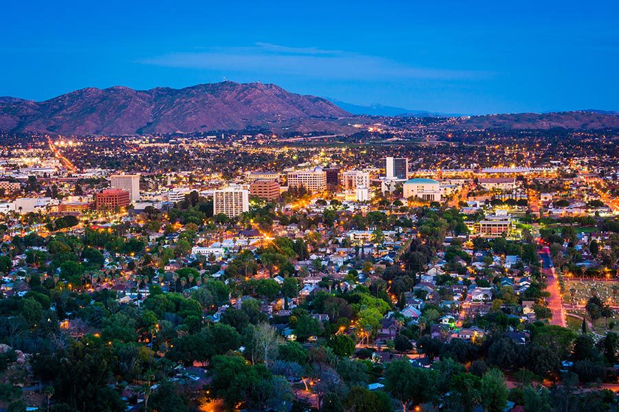 Riverside, CA Insurance - Riverside, California Seen From Above at Night, City Lit Up, Many Green Trees, and the Mountains Glowing Purple in the Distance